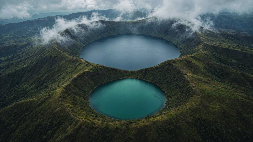 Aerial view of the Twin Muanenguba Lakes, one dark and one teal, fog on the crater rims